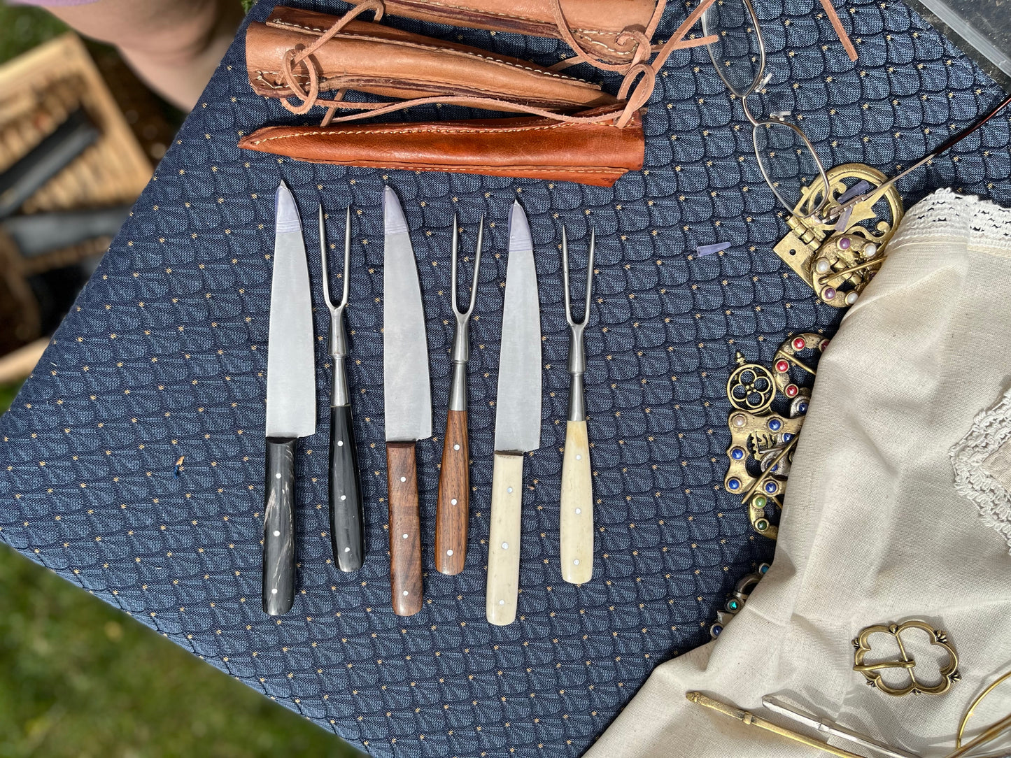Collection of medieval knives and forks with bone, horn, and wood handles, displayed with leather sheaths, perfect for reenactments and historical dining.